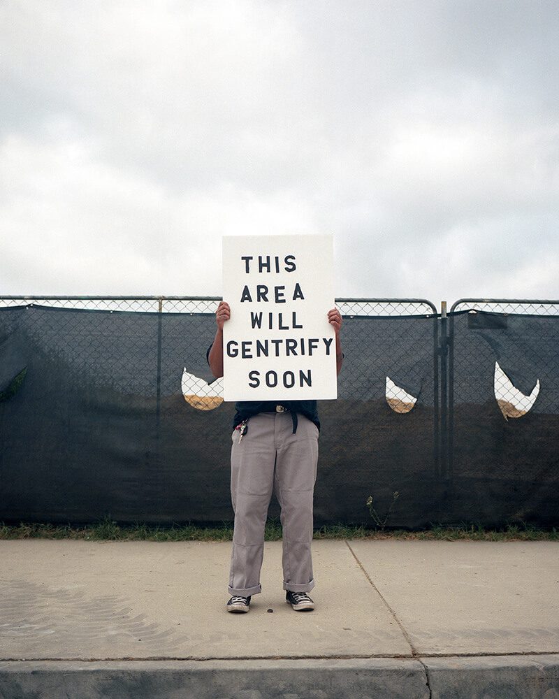 A man holding up a sign that says " this area will gentrify soon ".